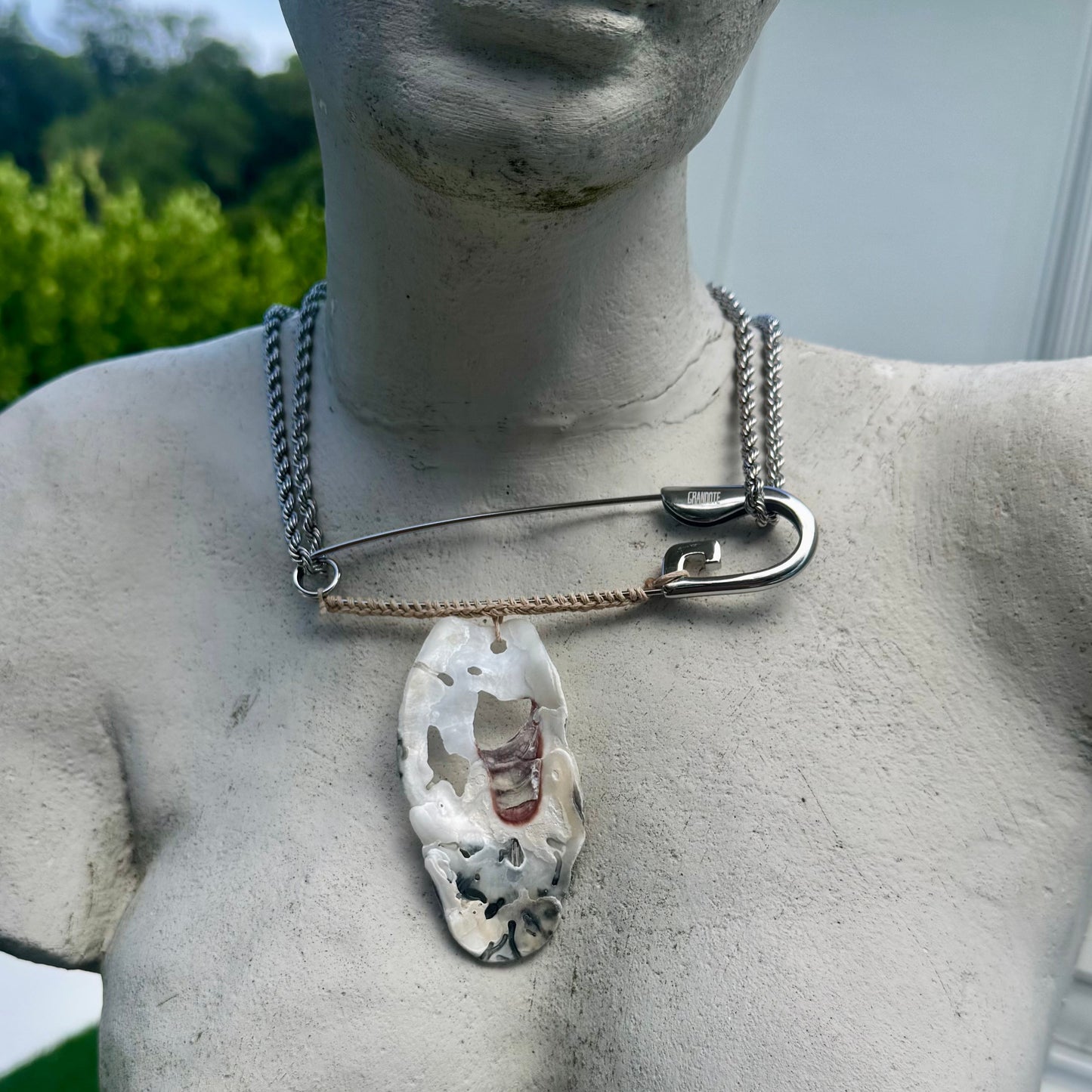 A custom silver necklace featuring a safety-pin style collar on a Venus statue outdoors.