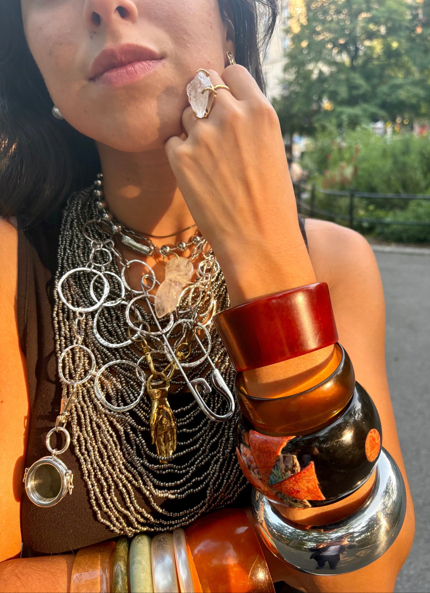 Person wearing multiple necklaces, charms, bangles, and bracelets outdoors. Showing maximalist stacking