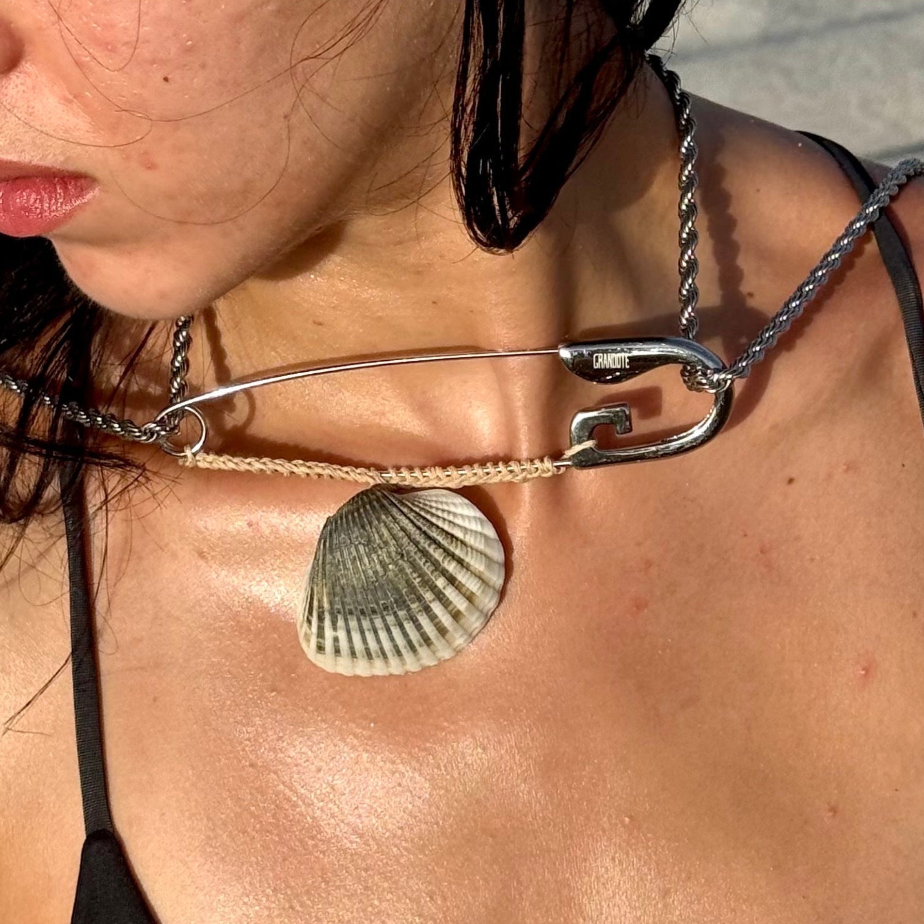 chunky silver chain necklace with a large shell pendant, photographed on the beach.