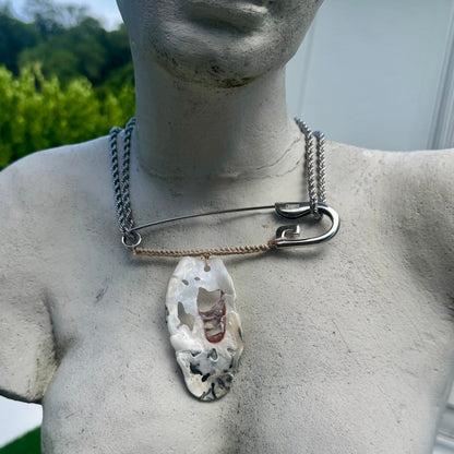 A custom silver necklace featuring a safety-pin style collar on a Venus statue outdoors.
