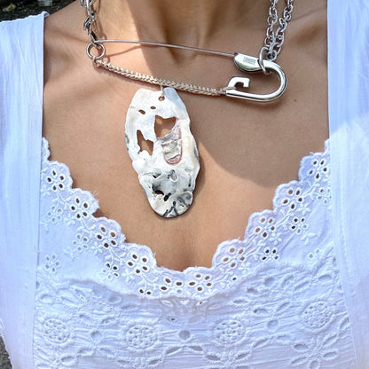 A close-up of a person wearing a white eyelet lace top and a silver necklace with a large, irregular white oyster shell pendant.