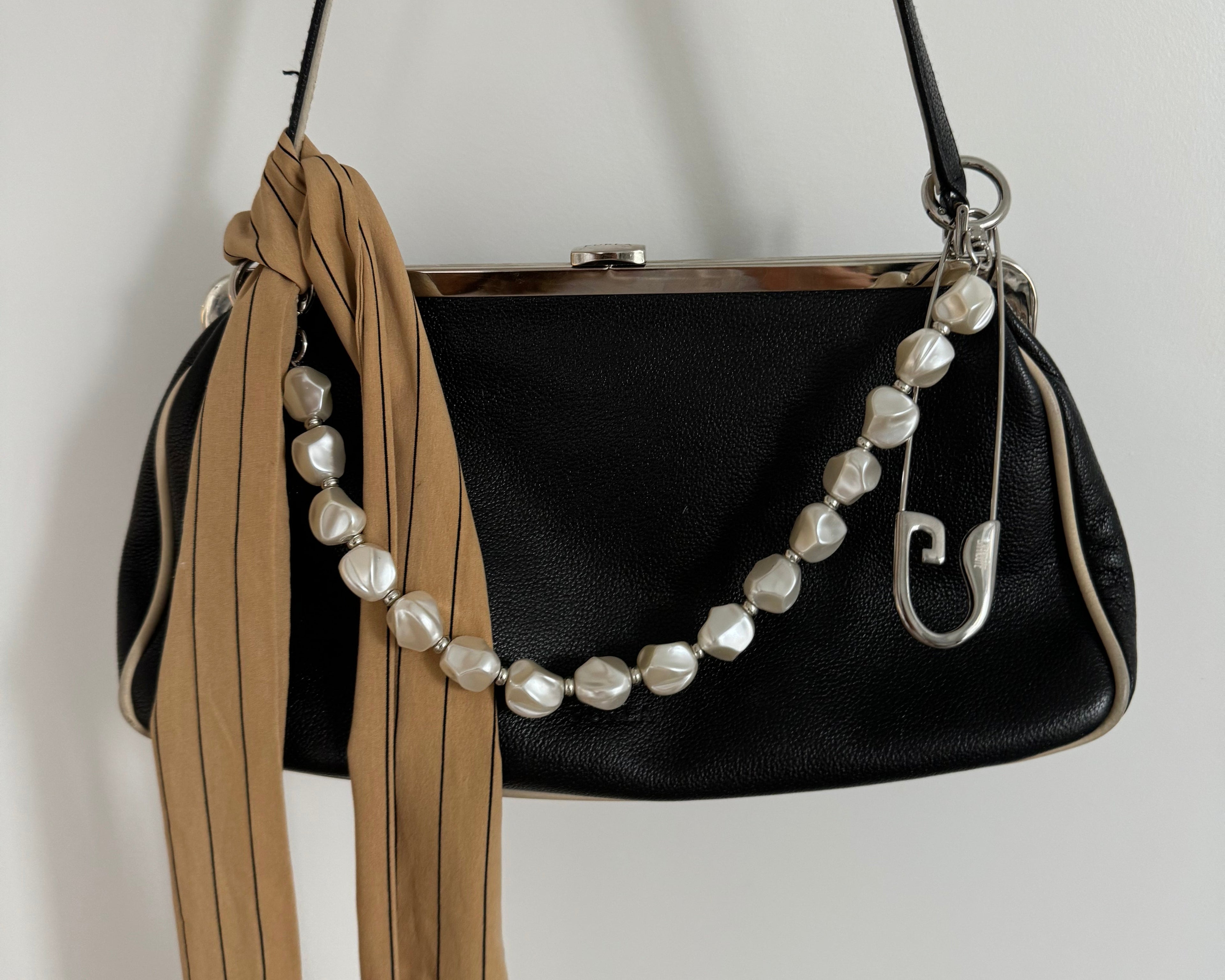 Black handbag with pearl strap on a light gray background and large safety pin